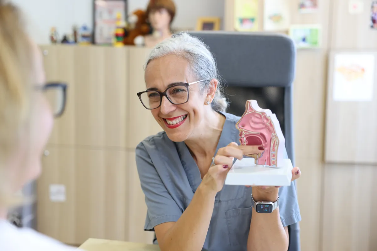 Therapeutin zeigt lächelnd ein anatomisches Modell von Mund und Rachen