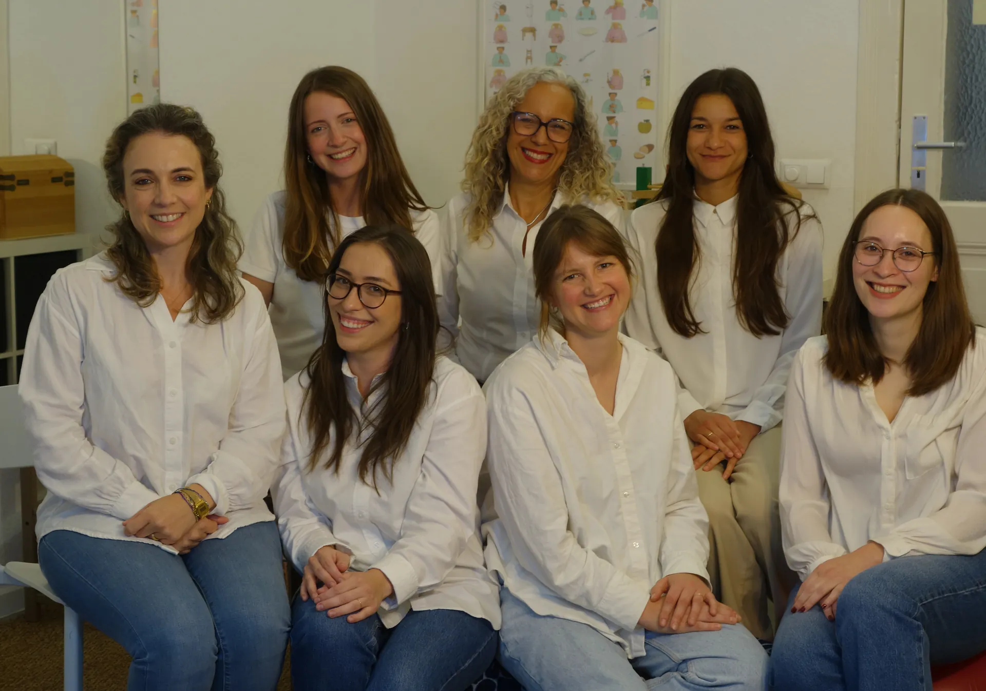 Das Team der Praxis in weißen Blusen, gemeinsam lächelnd im Therapieraum