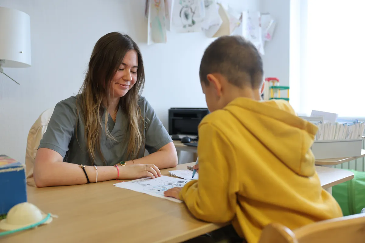 Therapeutin arbeitet am Tisch mit einem Jungen an einem Arbeitsblatt